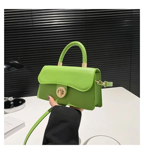 Detail of green satchel featuring wave flap design and golden circular metal twist lock