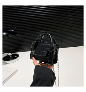 Close-up of black crocodile pattern mini bag with silver chain held in hand