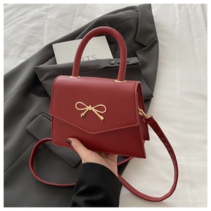 Close-up of red mini handbag with gold bow buckle on a dark grey blazer background