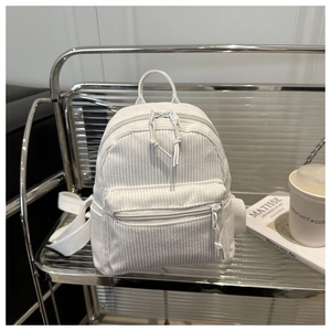 Detail view of white corduroy mini backpack showing vertical texture and front zipper pocket