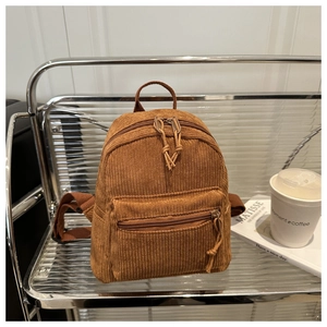 Detail of a brown corduroy backpack displayed on a shelf with art books and coffee