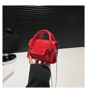Close-up of bright red mini bag featuring crocodile texture and metallic chain strap