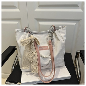 Close-up of white tote bag with pink leather straps, lace bows, and pearl chain details