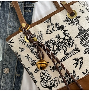 Detail of canvas bucket bag with floral print, leather handles, and golden bell charm