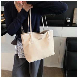 Detail of beige woven tote bag with slim shoulder strap and minimalist metal logo plate
