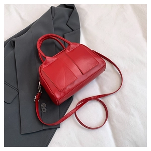 Detail of red Boston bag featuring matte leather texture on a grey blazer backdrop