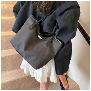 Detail of dark grey woven tote bag with leather handles shown in a lifestyle street setting