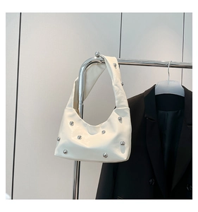 Close-up of white crossbody bag featuring silver ball rivet studs and wide shoulder strap
