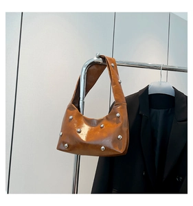 Close-up of brown glossy patent leather shoulder bag with silver rivet stud detailing