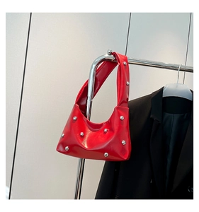 Detail of red glossy leather shoulder bag with silver rivet studs on cream background