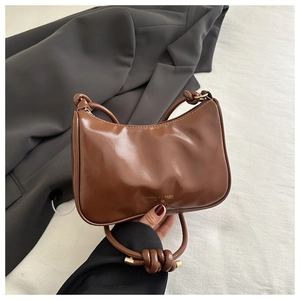 Detail of glossy brown leather shoulder bag with gold lettering and knotted strap detail