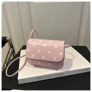 Détail du sac bandoulière rose à pois avec rabat posé sur un livre blanc