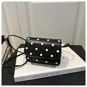 Détail du mini sac en cuir noir à pois blancs posé sur un livre élégant