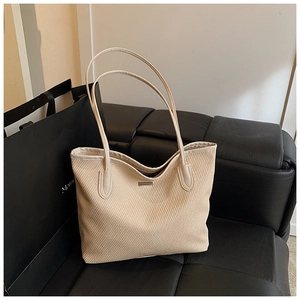 Detail of beige woven tote bag with slim handles on a leather sofa