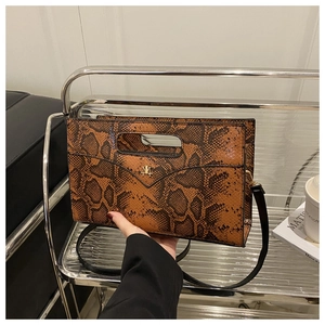 Detail of snake skin pattern handbag featuring gold metal logo and handle cutout