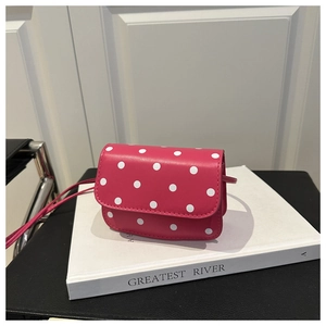 Gros plan d'un sac à bandoulière rose fuchsia à pois posé sur un livre blanc