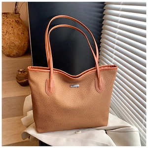 Detail view of woven brown tote bag featuring leather handles and rectangular metal logo