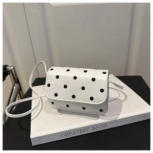 Détail du sac à bandoulière blanc à pois posé sur un livre dans un décor épuré