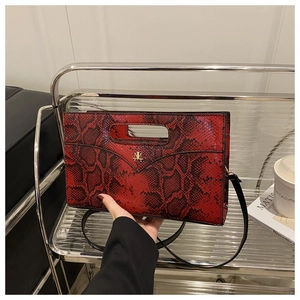 Detail showing red and black snakeskin texture and golden metal logo on the handbag