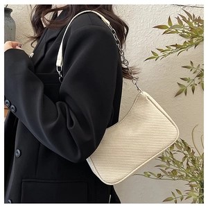 Détail du sac à bandoulière tissé blanc cassé avec chaîne argentée sur blazer noir