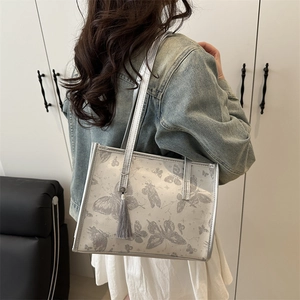Silver-grey tote bag with butterfly prints and tassel charm worn over shoulder