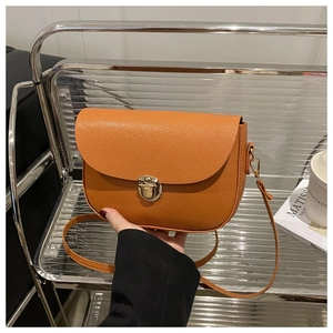 Detail of orange pebble leather crossbody bag featuring a gold round buckle and curved base