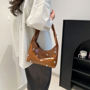 Caramel brown leather hobo bag with silver rivet studs worn as a shoulder bag