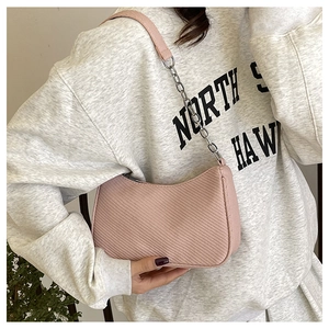 Detail of light pink shoulder bag with fine fabric texture and chain strap on a model