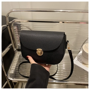 Close-up of black lychee grain leather saddle bag featuring a round golden metal lock buckle