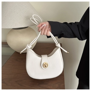 Dettaglio della borsa a mezzaluna beige con chiusura dorata e tracolla con nodo