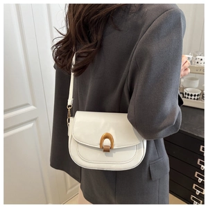 Détail du sac selle blanc avec boucle en U dorée porté sur un blazer gris