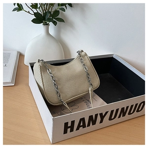 Détail du sac hobo tissé beige avec chaîne argentée sur un support de table épuré