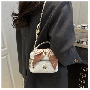 Detailed view of white quilted mini box bag with chain strap and camellia metal ornament