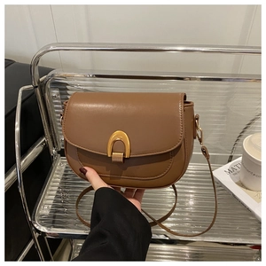 Gros plan d'un sac selle marron avec boucle en métal doré et bandoulière réglable