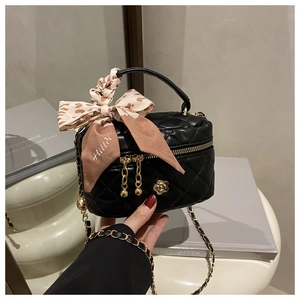 Close-up of black quilted box bag with gold flower badge and silk scarf handle detail