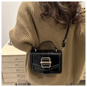 Detail of a black patent leather handbag with gold buckle styled on a brown sweater