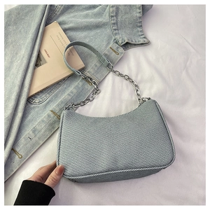 Détail du sac demi-lune en jean bleu clair avec bandoulière chaîne sur tissu blanc