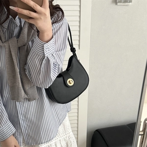 Sac bandoulière demi-lune noir minimaliste avec fermoir doré porté à l'épaule