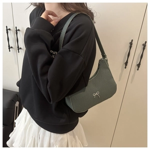 Close-up of a dark green woven shoulder bag featuring a silver metal bow detail