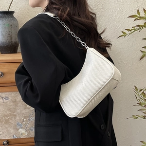 Sac à bandoulière tressé blanc avec chaîne en argent porté par un mannequin en intérieur