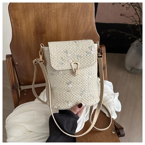 Détail de la broderie florale et du fermoir doré sur un sac à bandoulière en paille