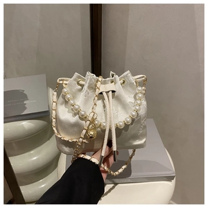 Detail of white jacquard satin bucket bag featuring pearl handle and gold chain strap