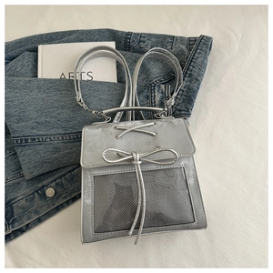 Detail of silver backpack featuring bow lacing and mesh pocket on denim background