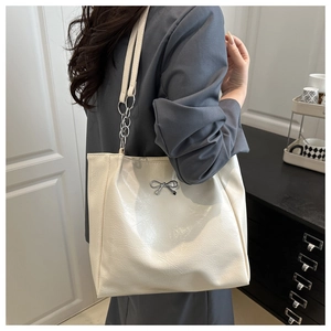 Detailed shot of cream tote bag with silver bow ornament and chain strap on shoulder