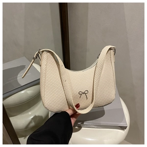 Detail of creamy white textured hobo bag with a silver metal bow accent and leather strap