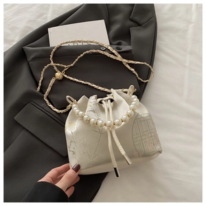 Detail of white silk bucket bag featuring bird embroidery and pearl beaded handle