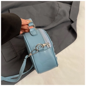 Detail of light blue denim patchwork bag featuring frayed fringe edges and silver zippers