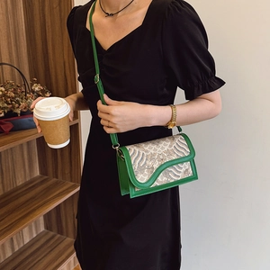Green embossed crossbody bag with vintage wave flap shown on black dress in casual setting