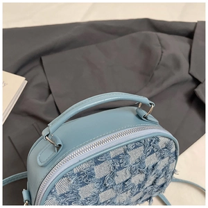 Close-up of light blue tweed mini handbag with fringe detail on a grey suit jacket