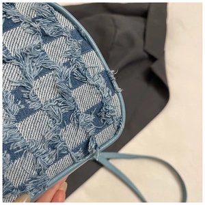 Detailed macro view of the checkered denim texture and frayed fringe edges on small square bag